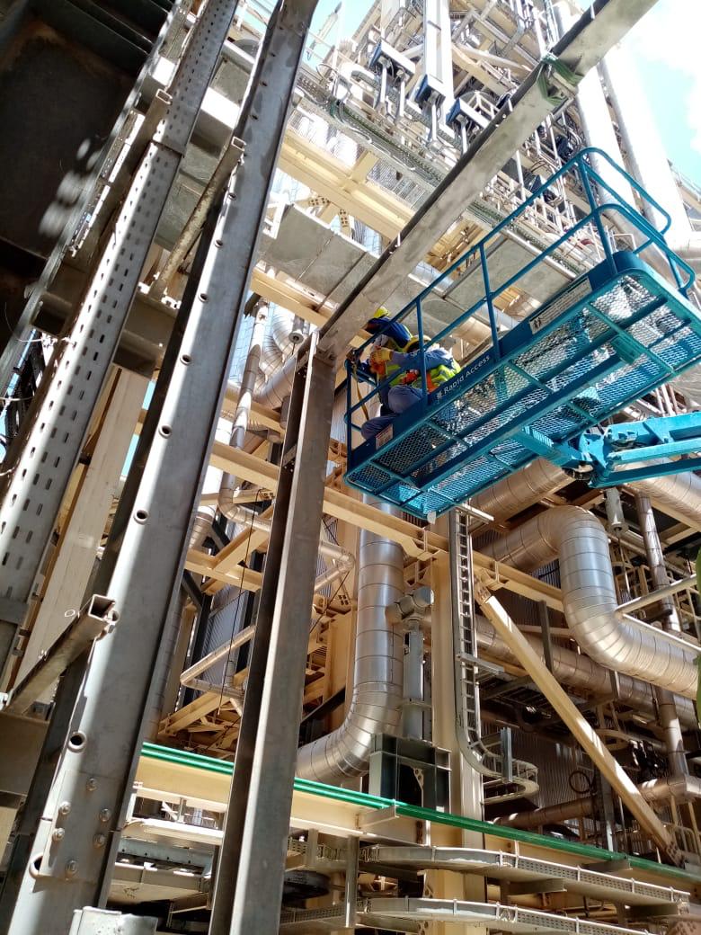 Worker on an elevated platform beside steel framing and insulated industrial piping