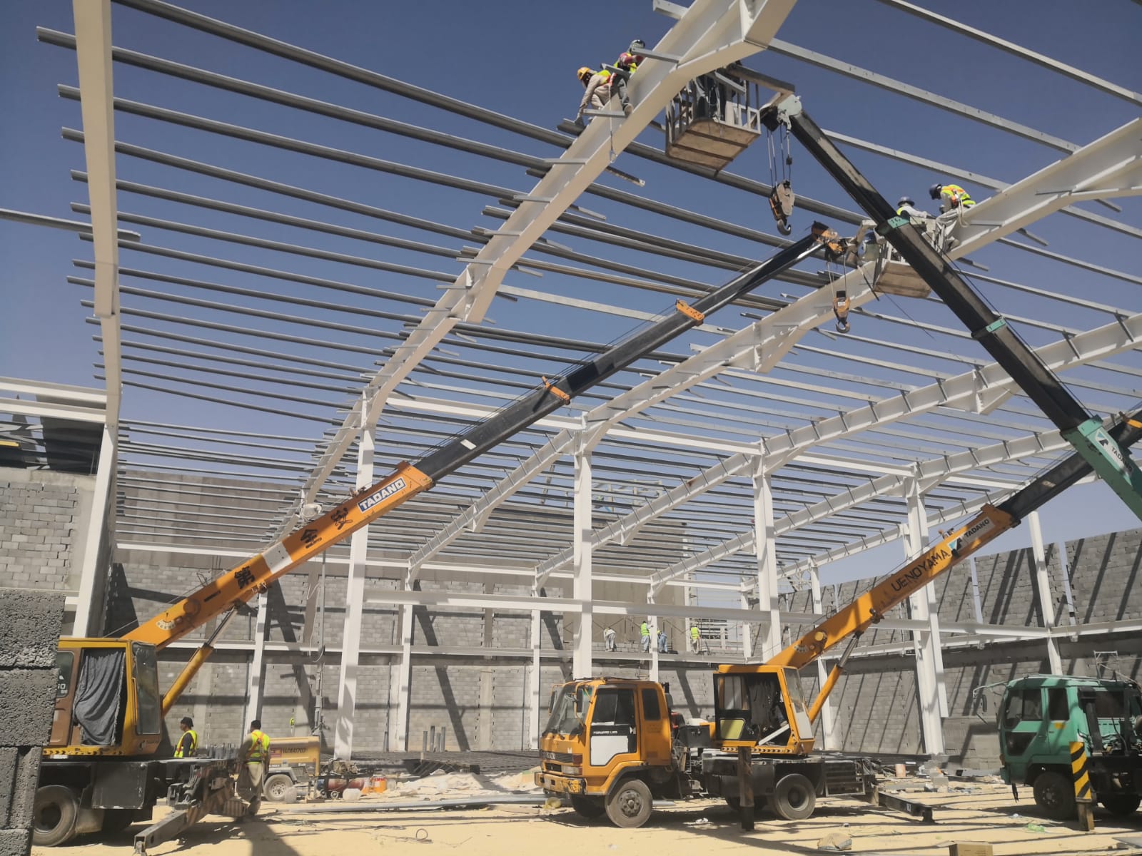 Workers installing steel roof members with lifting equipment
